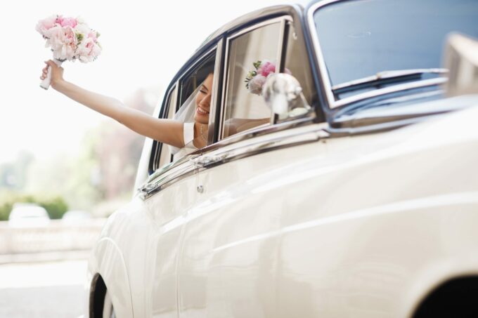 Beautiful bride sits with wedding bouquet in a retro car and has